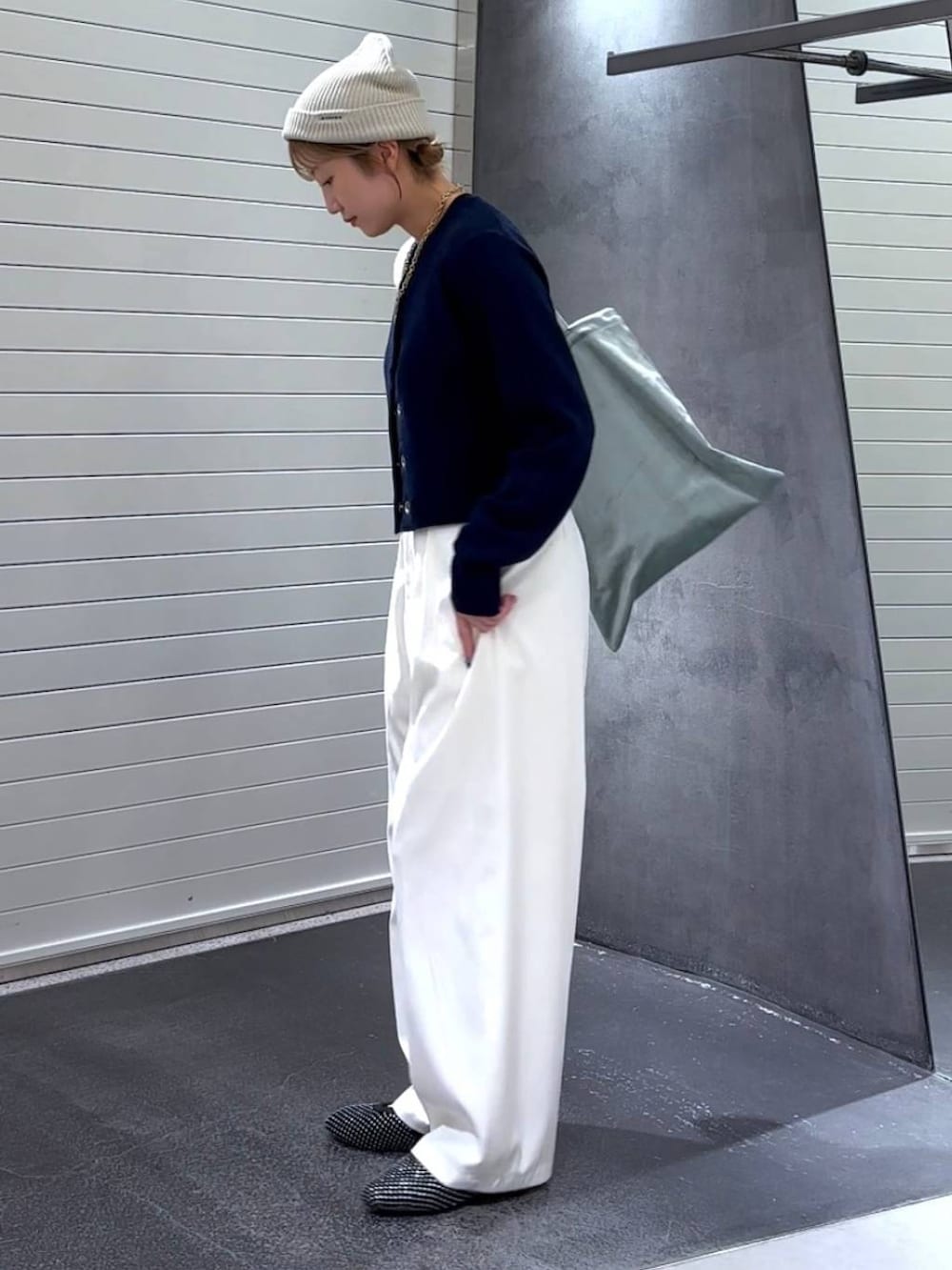 グリーン系のトートバッグ、ブラック系のパンプス、ホワイト系のスラックスを着用したレディースの秋コーディネートの6枚目の写真