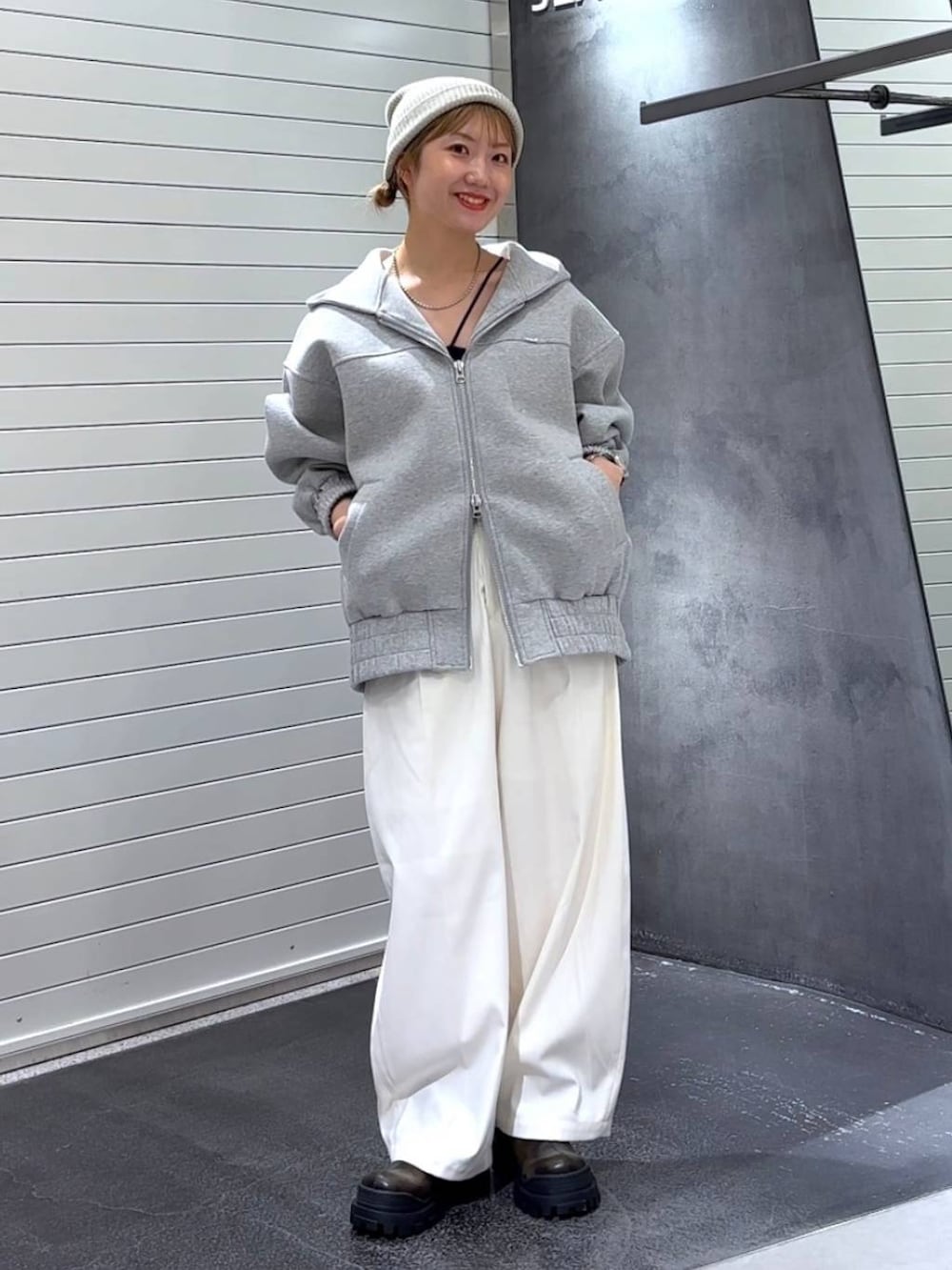 グレー系のパーカー、グリーン系のブーツ、ホワイト系のスラックスを着用したレディースの秋コーディネートの3枚目の写真