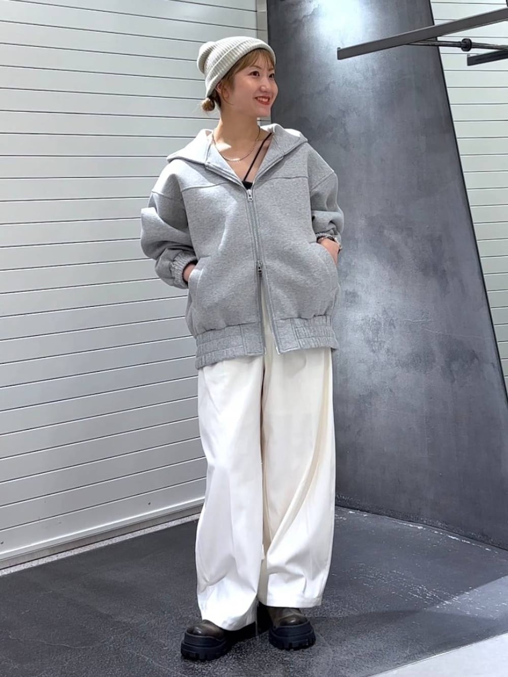 グレー系のパーカー、グリーン系のブーツ、ホワイト系のスラックスを着用したレディースの秋コーディネートの2枚目の写真