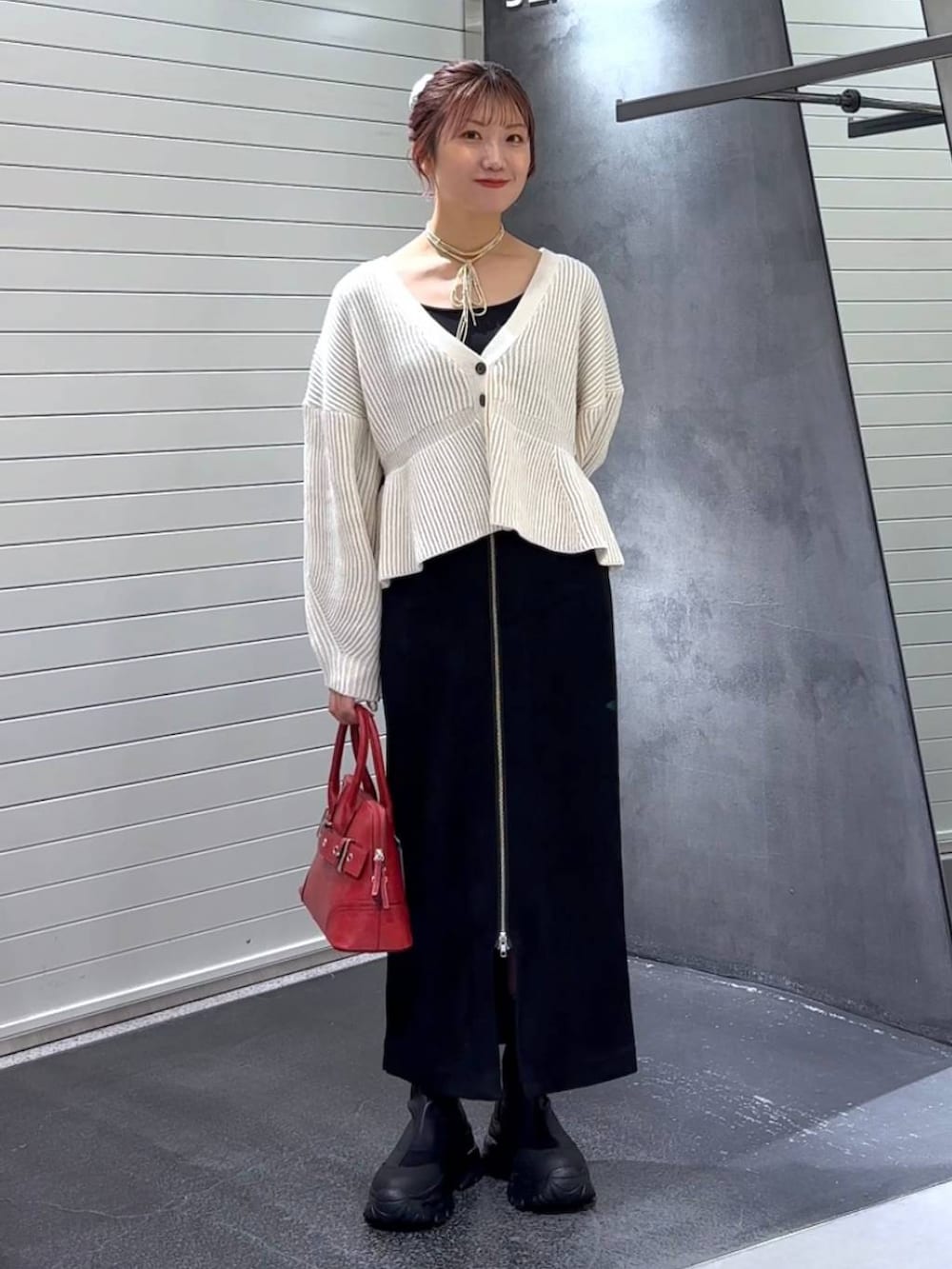 ブラック系のスカート、ブラック系のブーツ、レッド系のボストンバッグを着用したレディースの秋コーディネートの2枚目の写真
