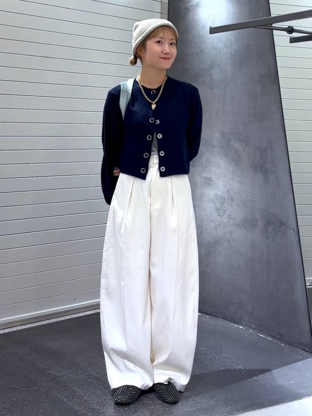 グリーン系のトートバッグ、ブラック系のパンプス、ホワイト系のスラックスを着用したレディースの秋コーディネートの2枚目の写真