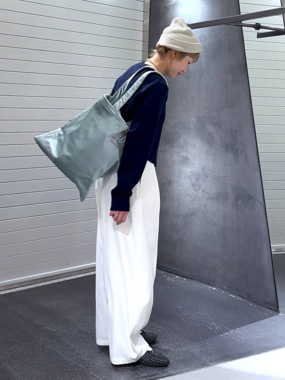 グリーン系のトートバッグ、ブラック系のパンプス、ホワイト系のスラックスを着用したレディースの秋コーディネートの4枚目の写真