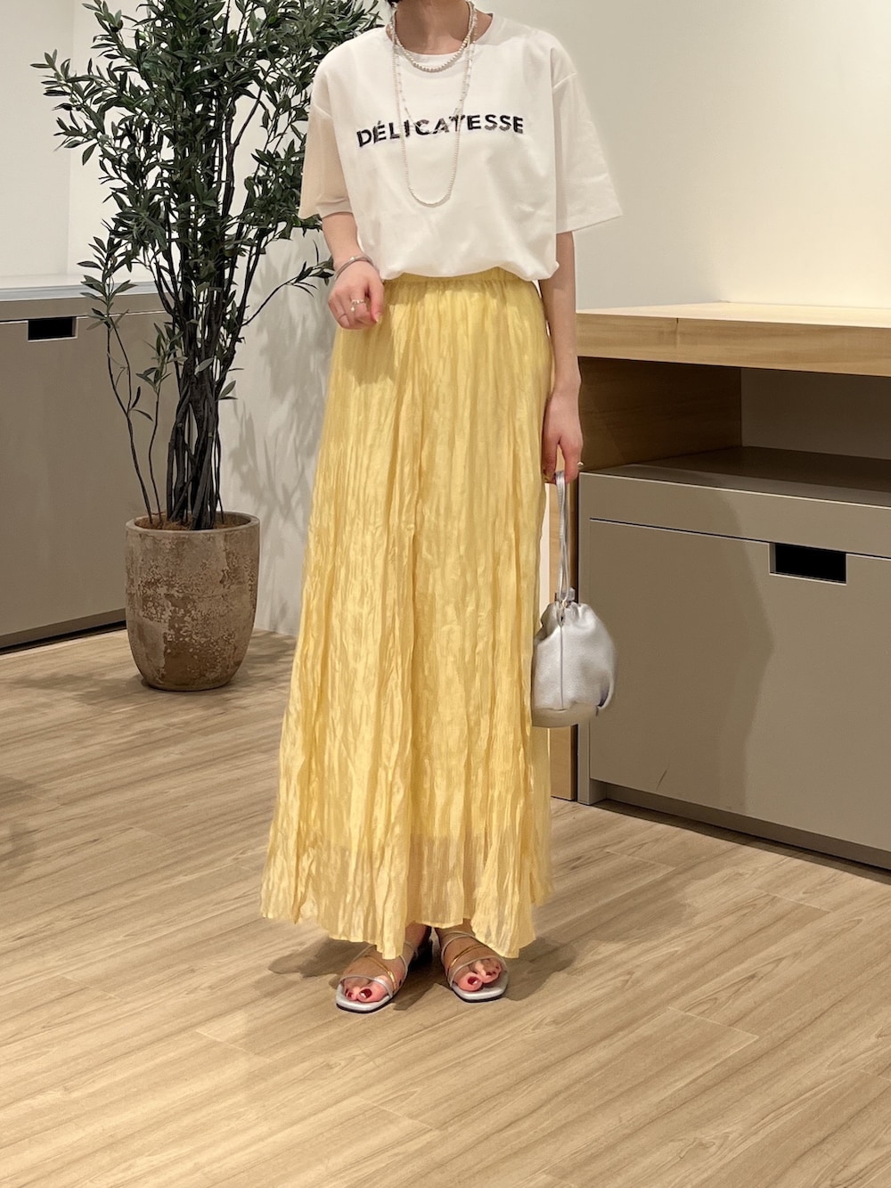 イエロー系のスカート、シルバー系のトートバッグ、シルバー系のサンダルを着用したレディースの夏コーディネートの2枚目の写真