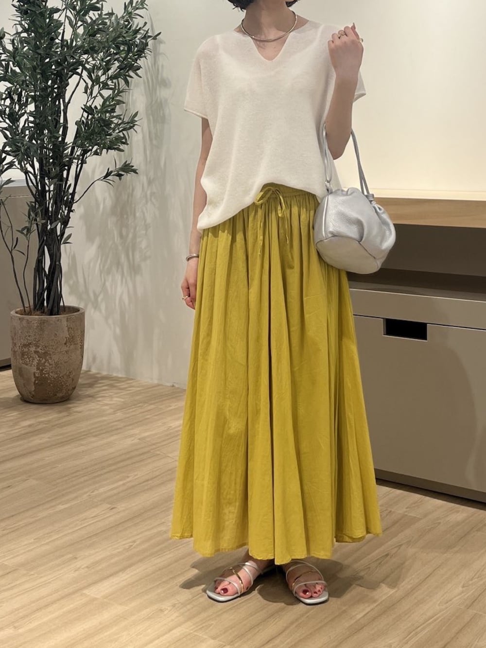 ホワイト系のニット/セーター、イエロー系のスカート、シルバー系のトートバッグを着用したレディースの夏コーディネートの2枚目の写真