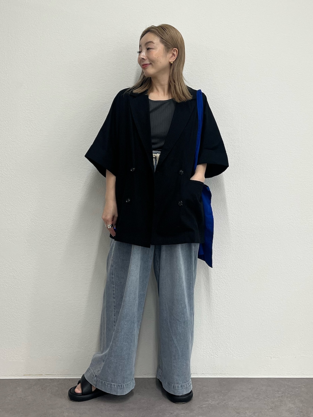 ブラック系のテーラードジャケット、ブルー系のデニムパンツ、ブラック系のサンダルを着用したレディースの夏コーディネートの2枚目の写真