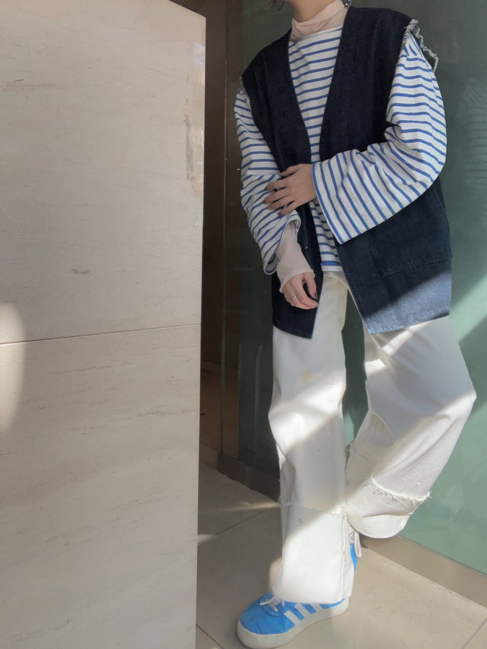 ホワイト系のデニムパンツ、ブルー系のスニーカー、ブルー系のベストを着用したレディースの春コーディネートの2枚目の写真