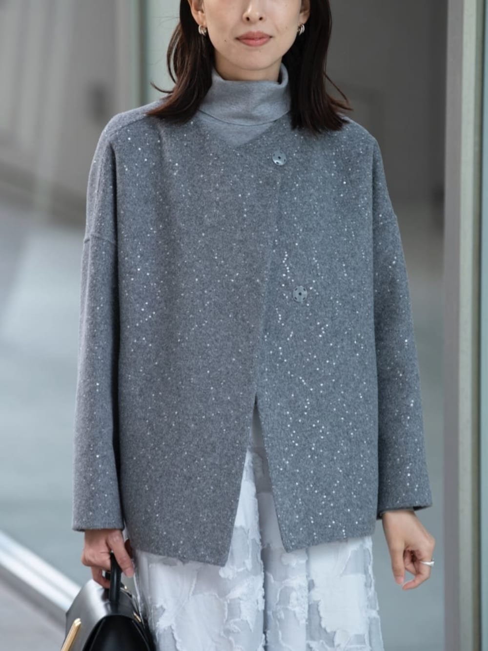 グレー系のノーカラーコート、グレー系のニット/セーター、ブルー系のスカートを着用したレディースの秋コーディネートの2枚目の写真