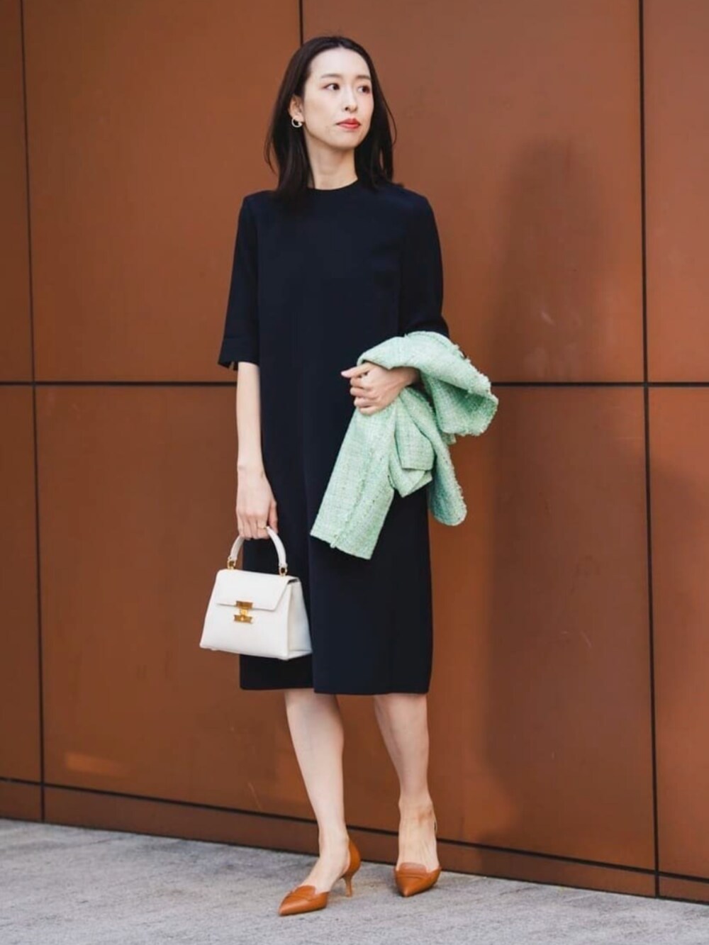 グリーン系のノーカラージャケット、ブラック系のワンピース、ゴールド系のイヤリングを着用したレディースの冬コーディネートの3枚目の写真