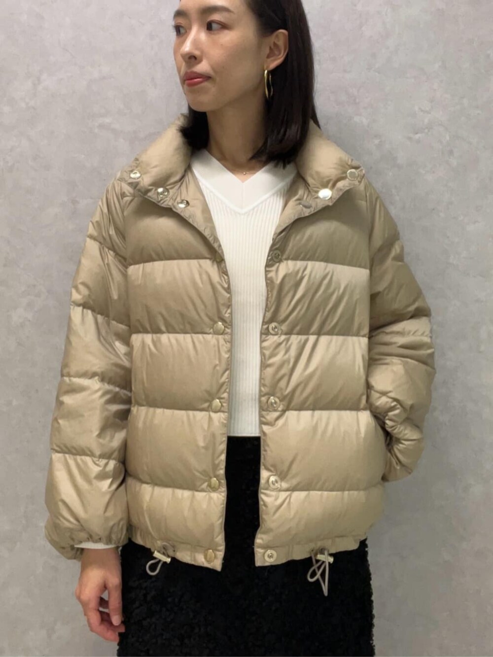 ブラック系のショルダーバッグ、ベージュ系のダウンジャケット/コート、ホワイト系のニット/セーターを着用したレディースの冬コーディネートの2枚目の写真