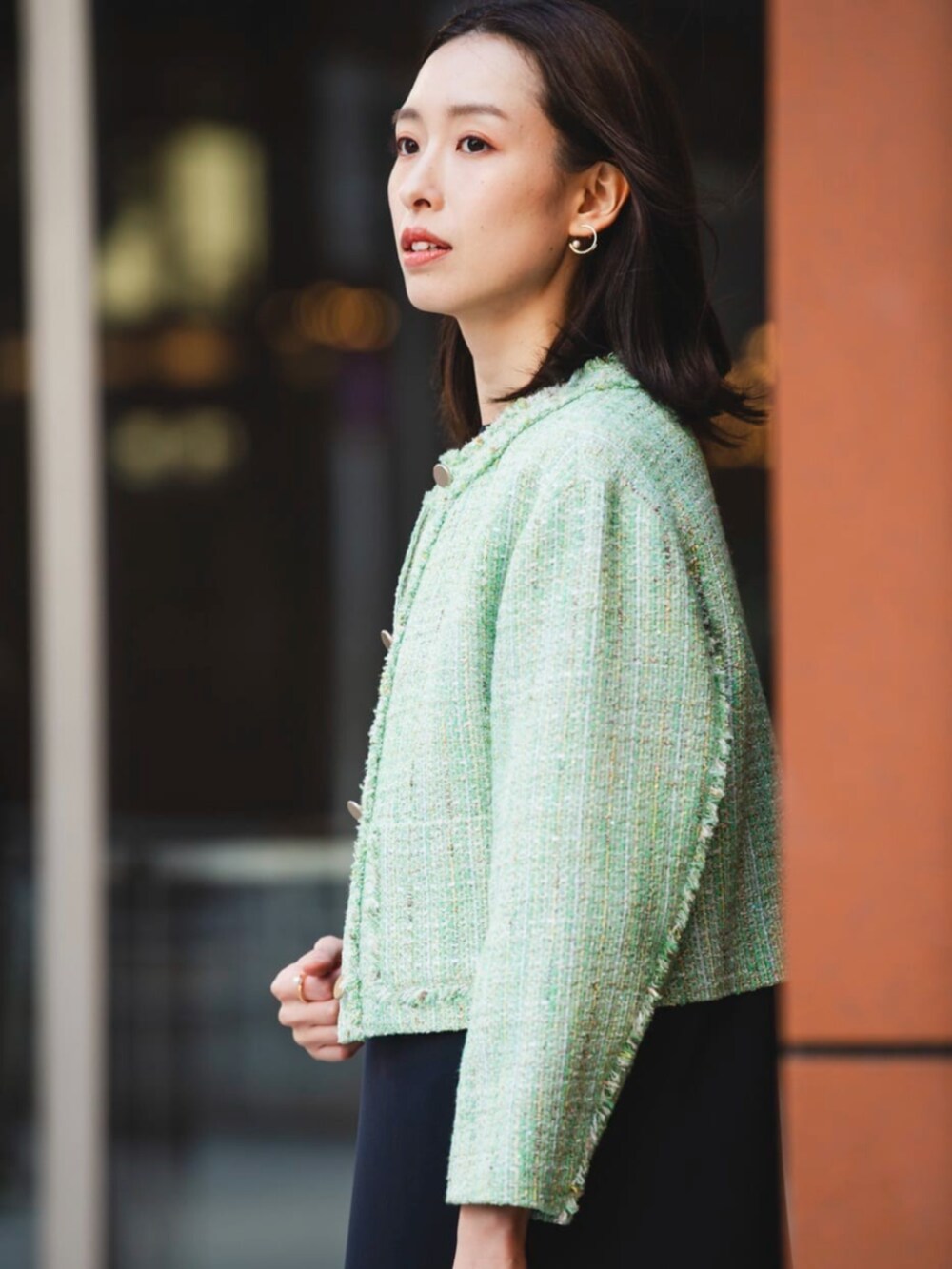 グリーン系のノーカラージャケット、ブラック系のワンピース、ゴールド系のイヤリングを着用したレディースの冬コーディネートの5枚目の写真