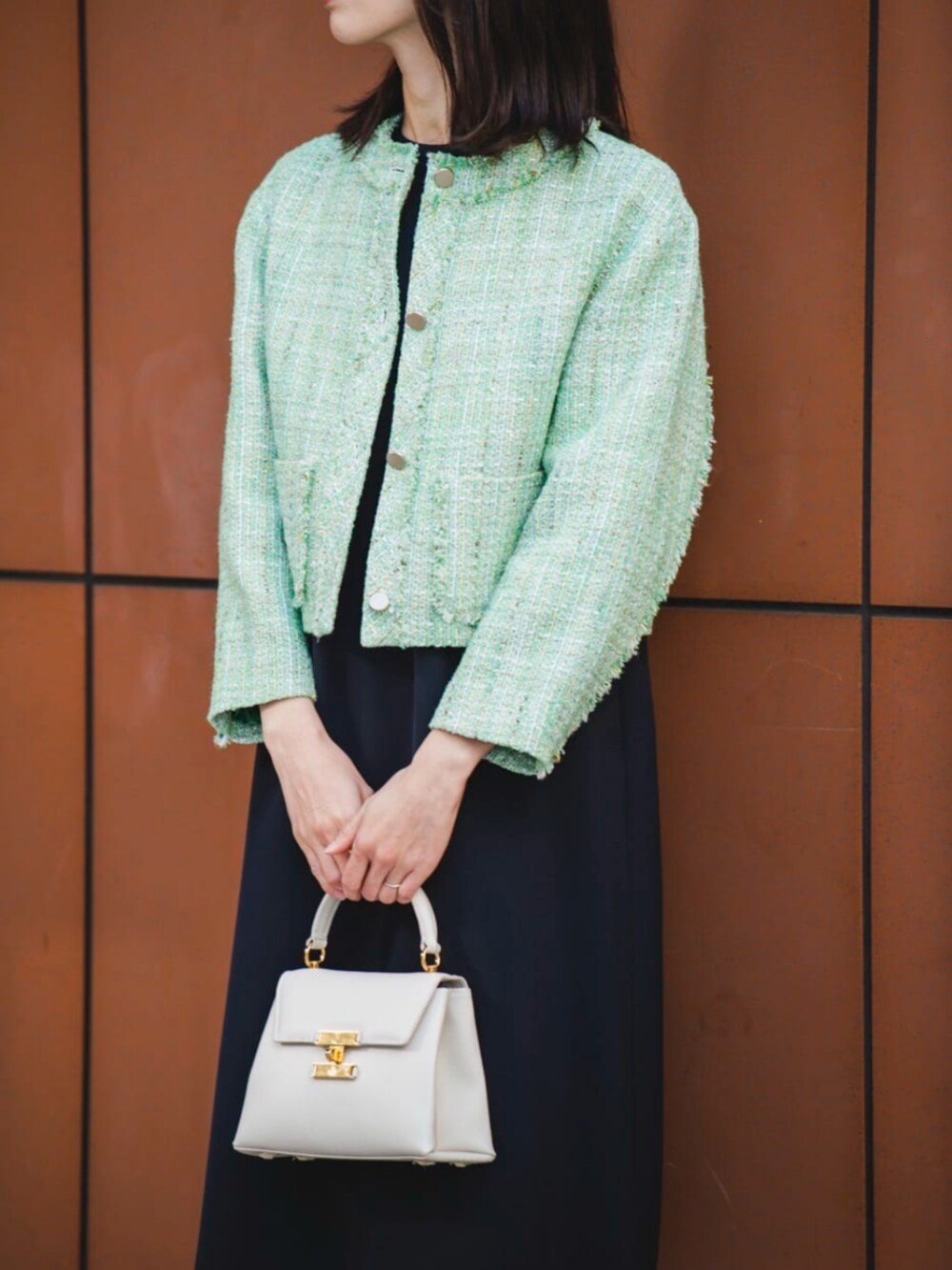 グリーン系のノーカラージャケット、ブラック系のワンピース、ゴールド系のイヤリングを着用したレディースの冬コーディネートの2枚目の写真