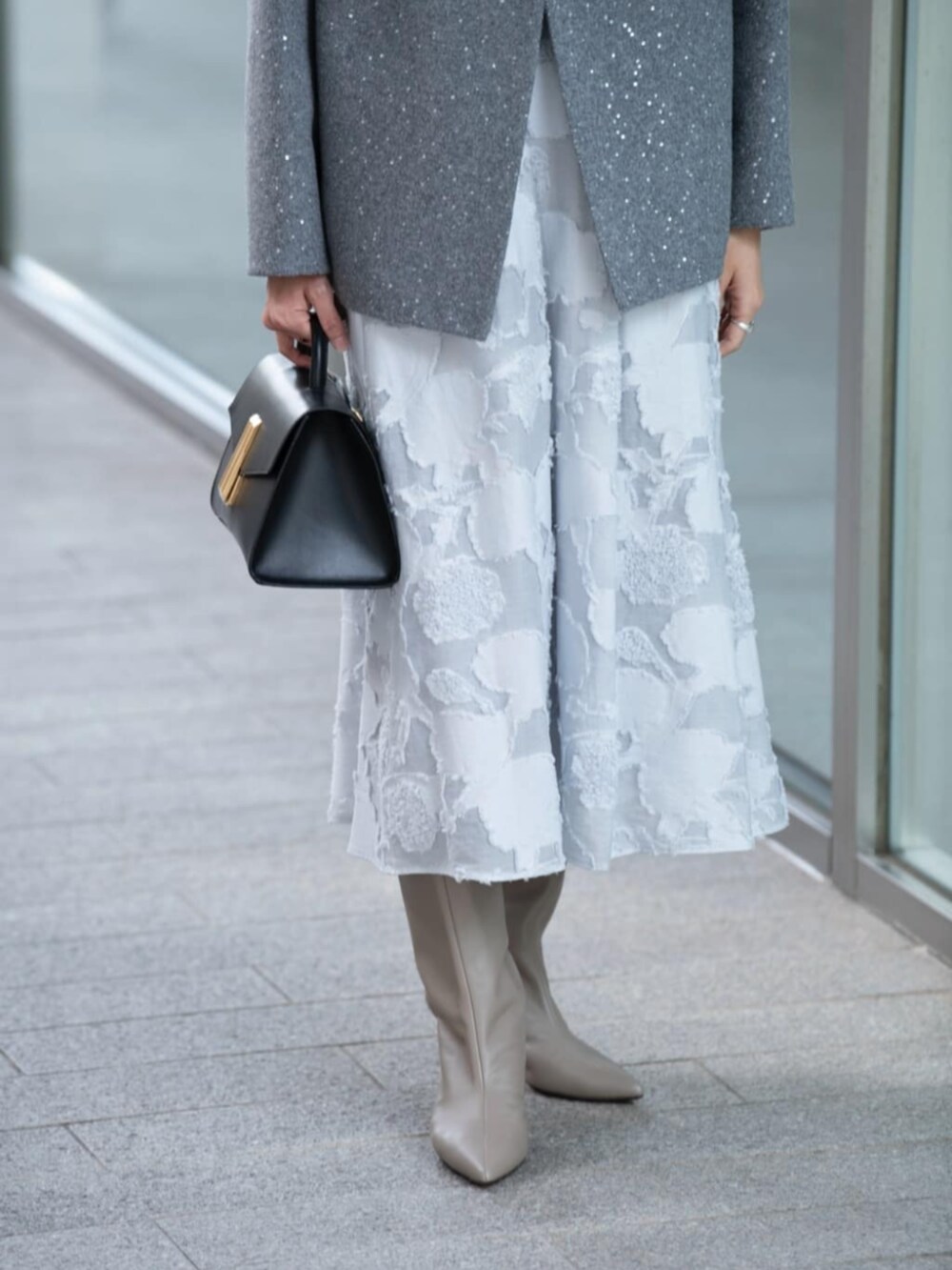 グレー系のノーカラーコート、グレー系のニット/セーター、ブルー系のスカートを着用したレディースの秋コーディネートの3枚目の写真