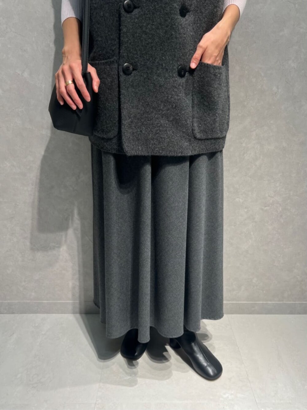 グレー系のベスト、ピンク系のニット/セーター、グレー系のスカートを着用したレディースの秋コーディネートの3枚目の写真