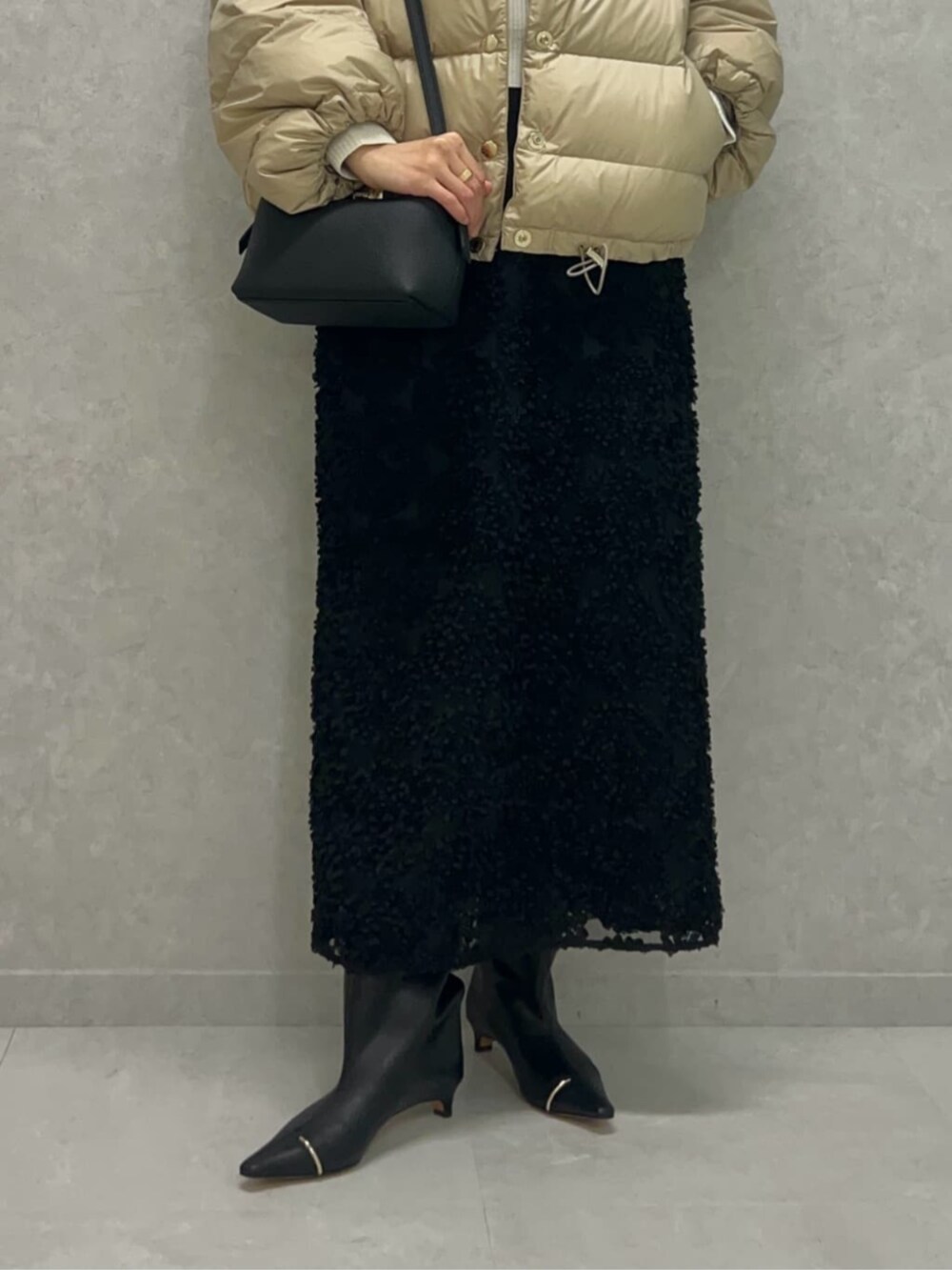 ブラック系のショルダーバッグ、ベージュ系のダウンジャケット/コート、ホワイト系のニット/セーターを着用したレディースの冬コーディネートの3枚目の写真