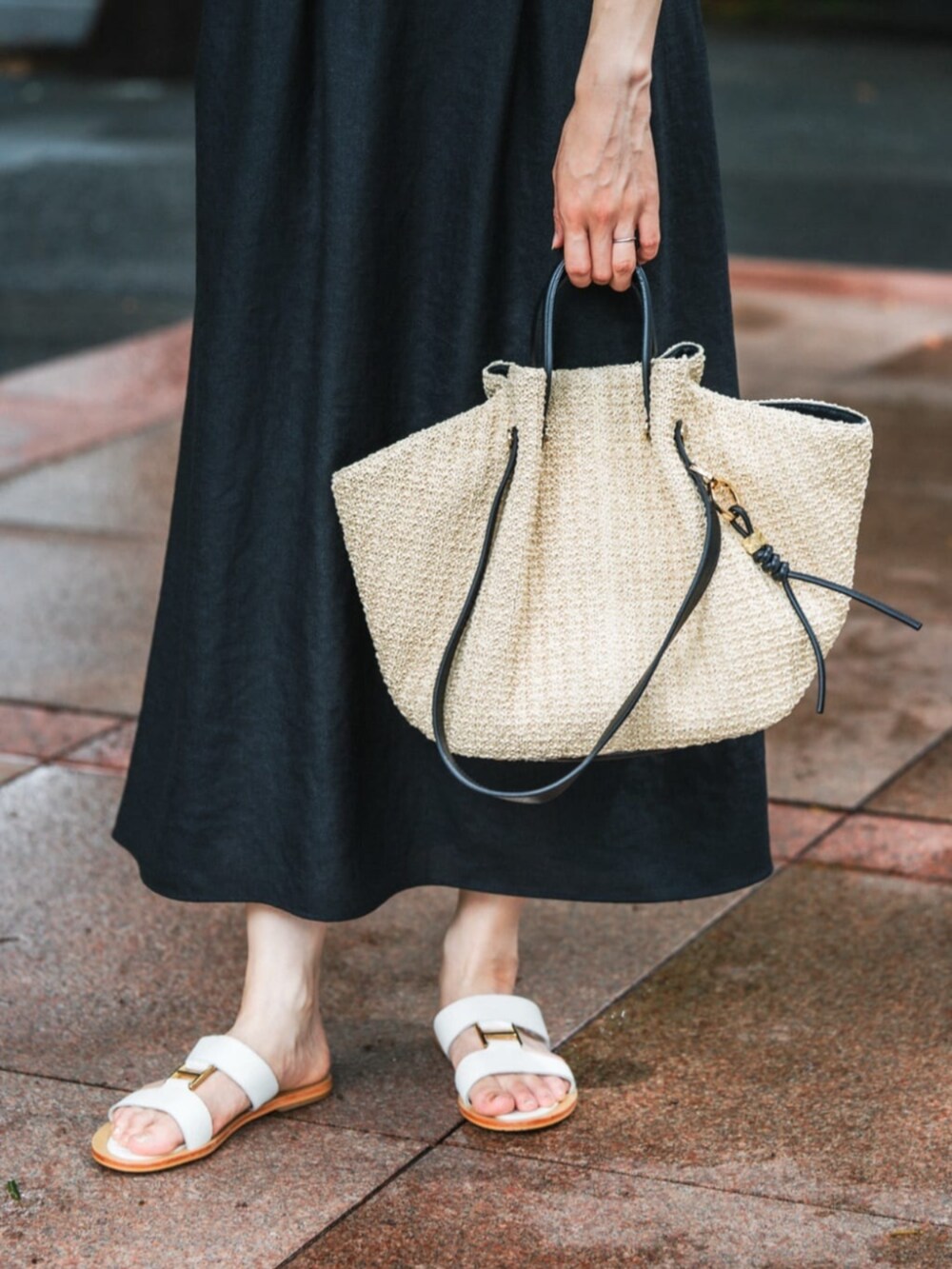 ブラック系のワンピース、ホワイト系のサンダル、ベージュ系のかごバッグを着用したレディースの夏コーディネートの3枚目の写真
