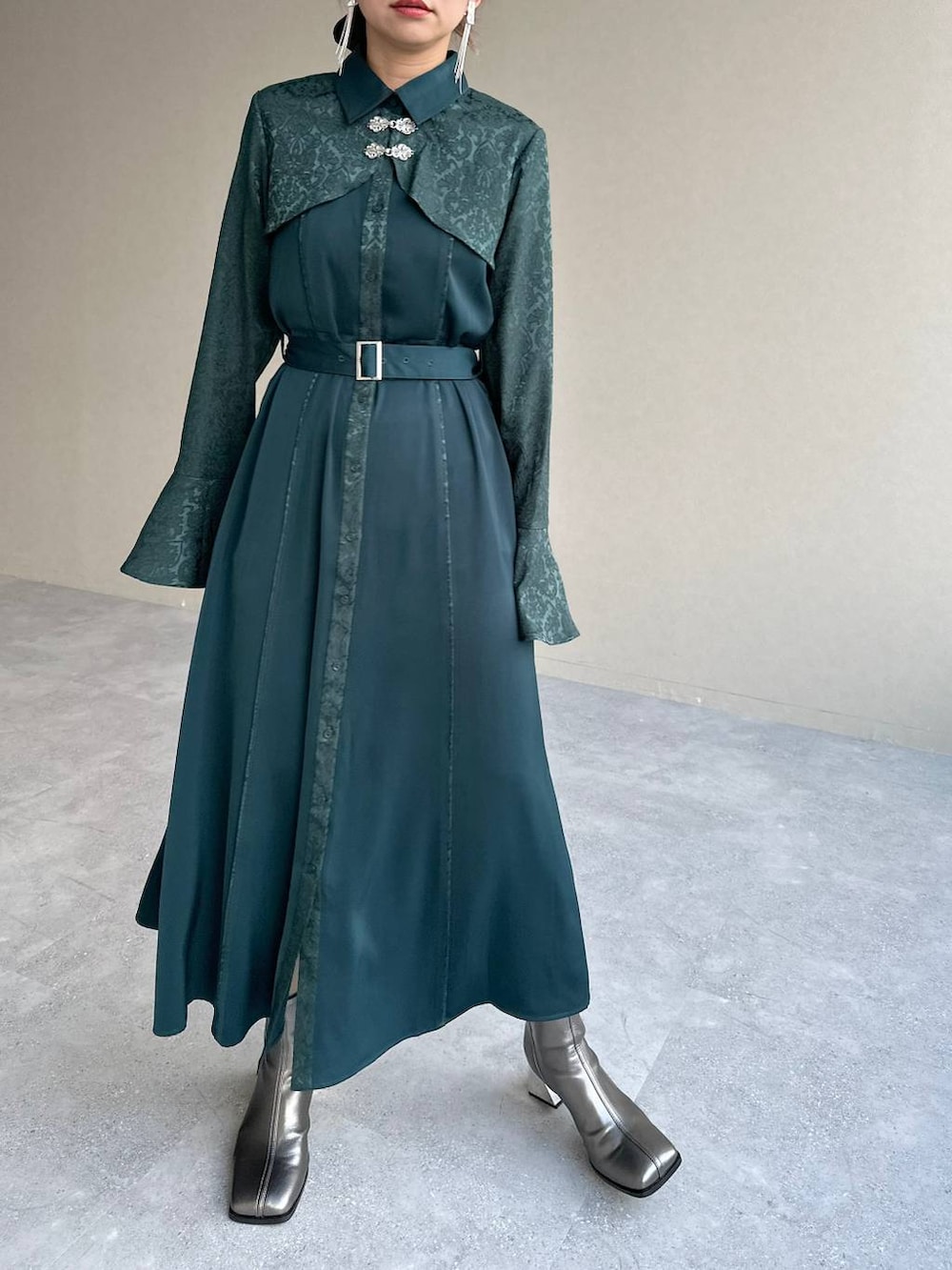 シルバー系のブーツ、グリーン系のワンピース、シルバー系のイヤリングを着用したレディースの秋コーディネートの4枚目の写真