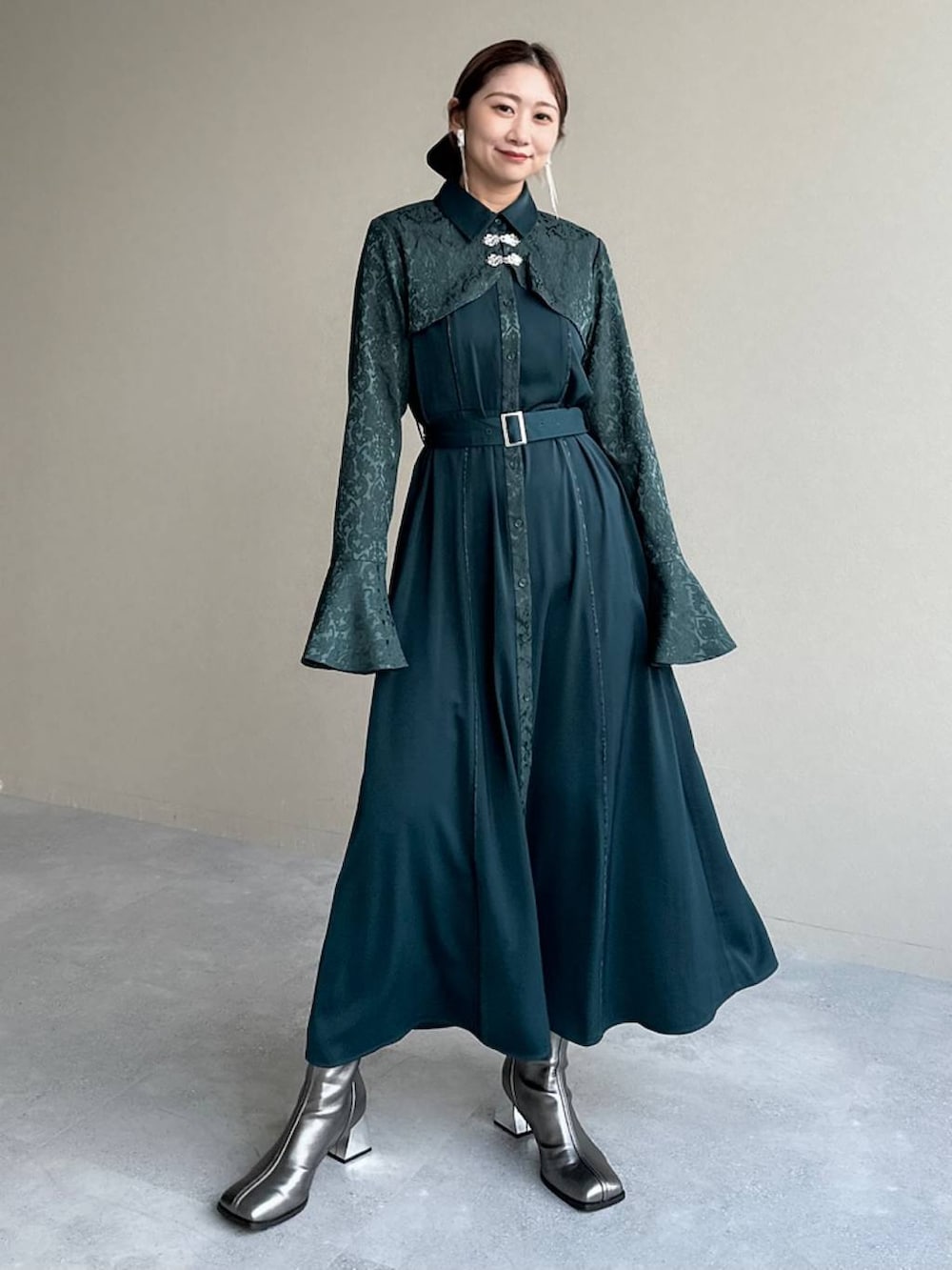 シルバー系のブーツ、グリーン系のワンピース、シルバー系のイヤリングを着用したレディースの秋コーディネートの7枚目の写真