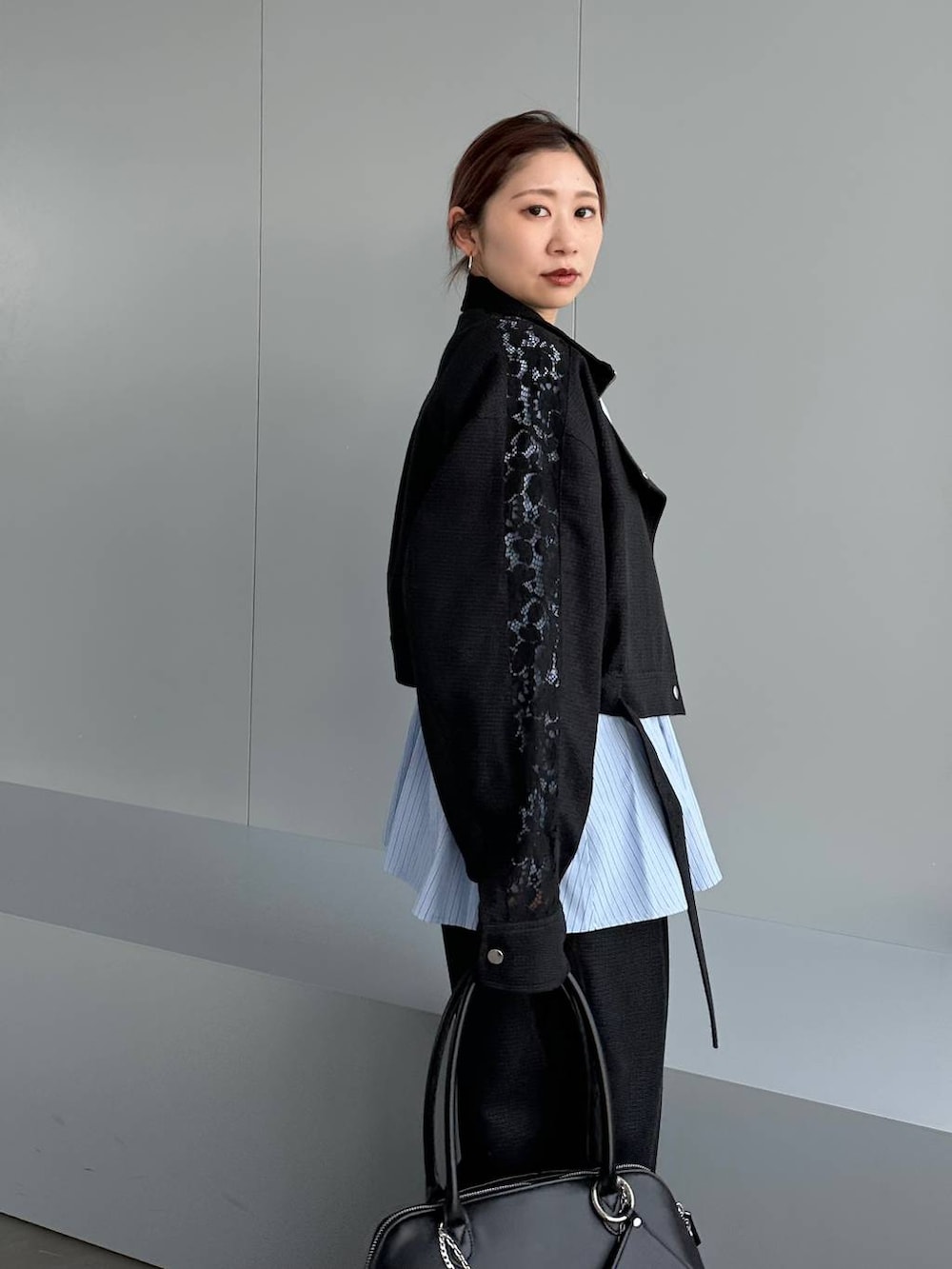 ブラック系のハンドバッグ、ブラック系のスラックス、ブラック系のブルゾンを着用したレディースの春コーディネートの5枚目の写真