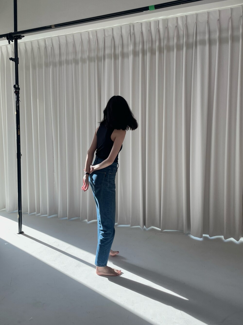 ブラック系のタンクトップ、ブルー系のデニムパンツ、ゴールド系のネックレスを着用したレディースの夏コーディネートの2枚目の写真