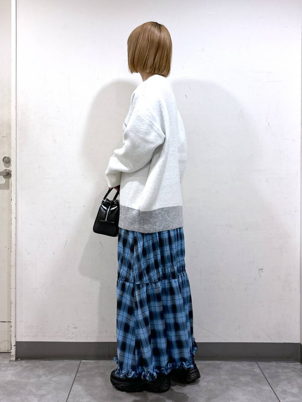 ブラック系のブーツ、ブルー系のスカート、ブラック系のボストンバッグを着用したレディースの秋コーディネートの2枚目の写真