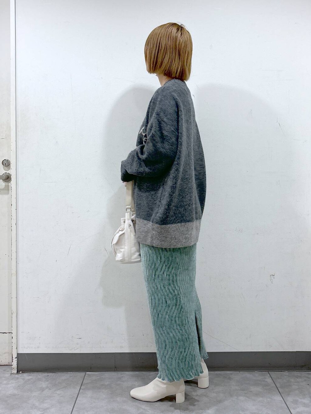 グレー系のニット/セーター、グリーン系のスカート、ホワイト系のショルダーバッグを着用したレディースの秋コーディネートの3枚目の写真