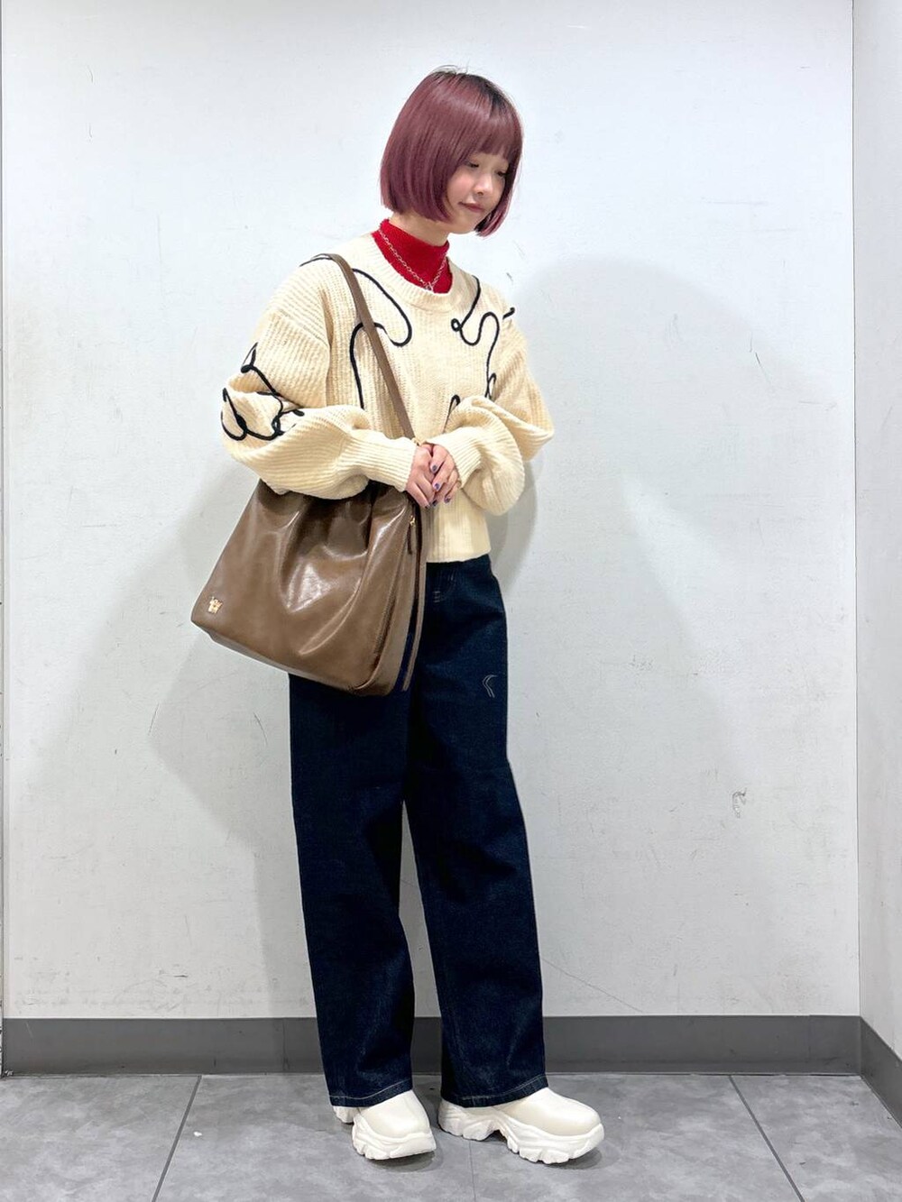 レッド系のニット/セーター、ホワイト系のブーツ、ブラウン系のショルダーバッグを着用したレディースの冬コーディネートの2枚目の写真