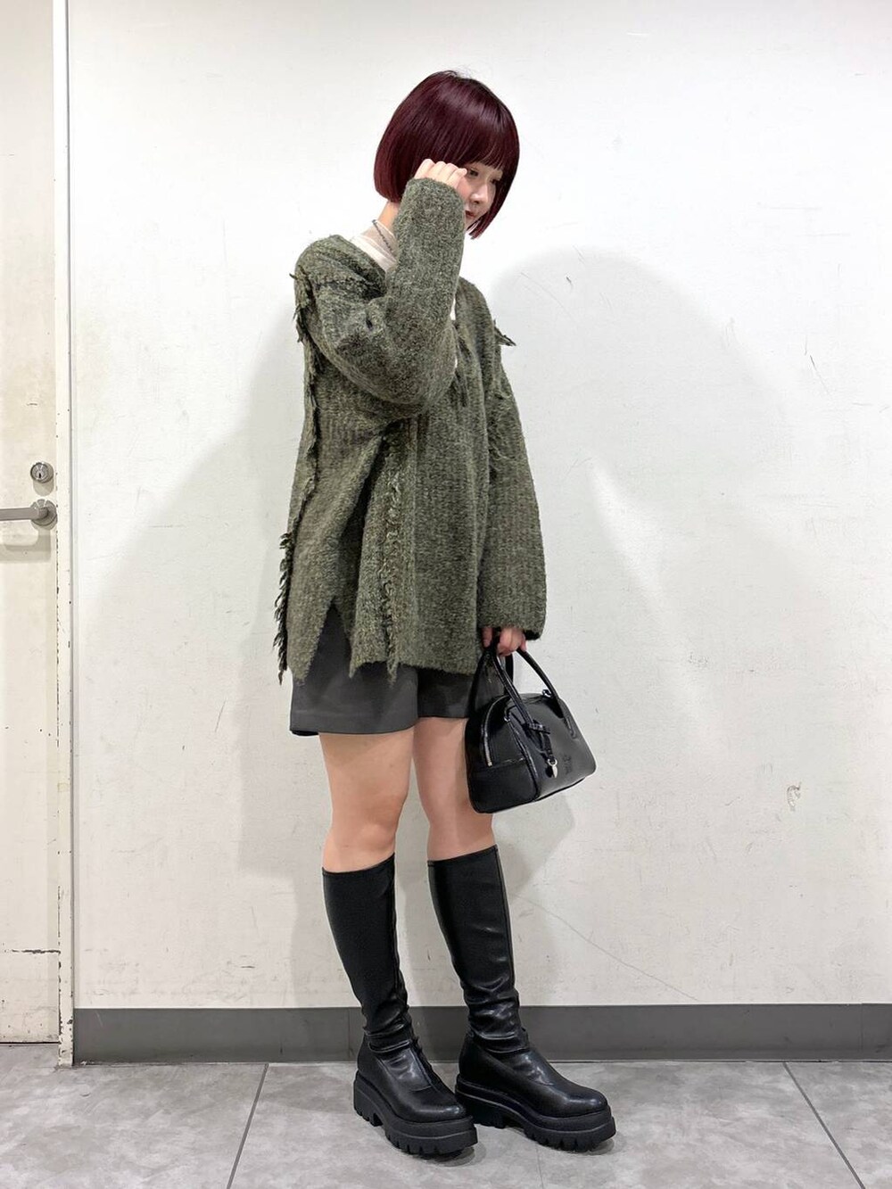 グリーン系のニット/セーター、ブラック系のブーツ、ブラック系のボストンバッグを着用したレディースの秋コーディネートの2枚目の写真