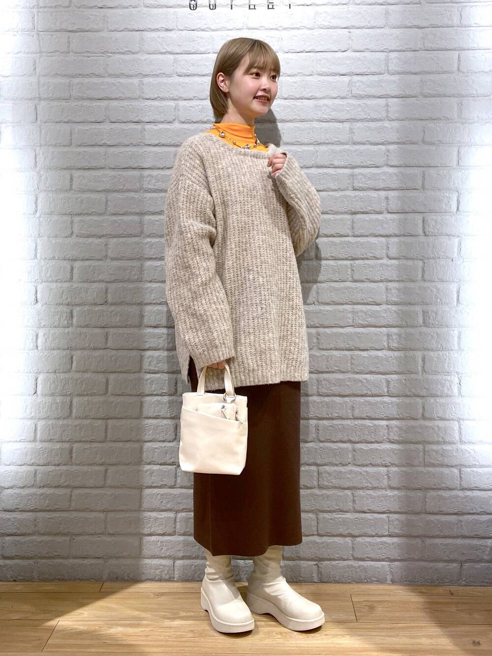 オレンジ系のTシャツ/カットソー、ホワイト系のブーツ、ブラウン系のスカートを着用したレディースの冬コーディネートの3枚目の写真