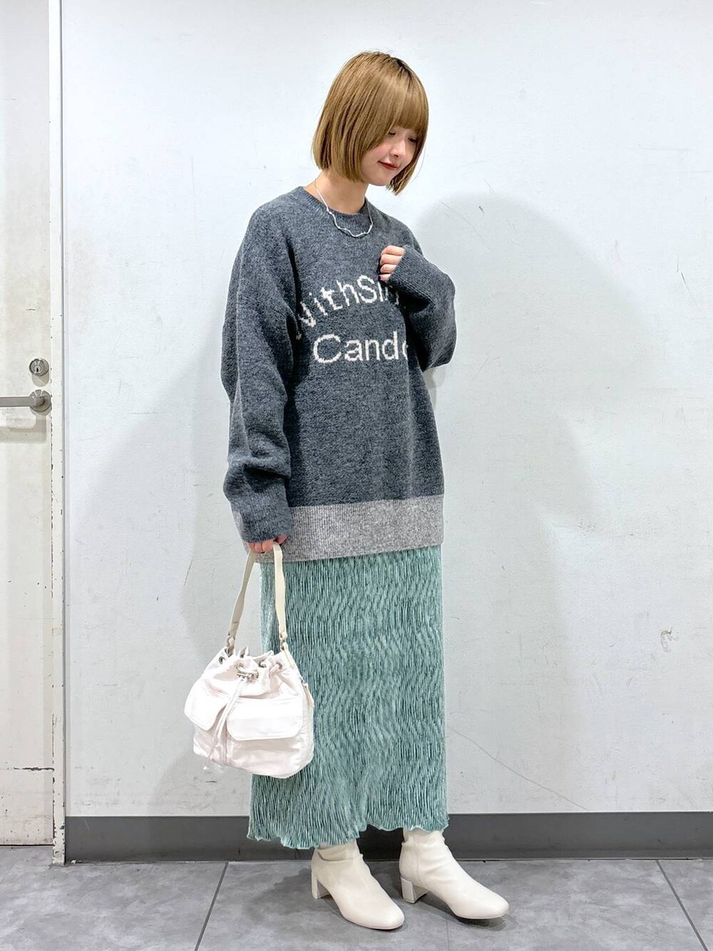グレー系のニット/セーター、グリーン系のスカート、ホワイト系のショルダーバッグを着用したレディースの秋コーディネートの2枚目の写真