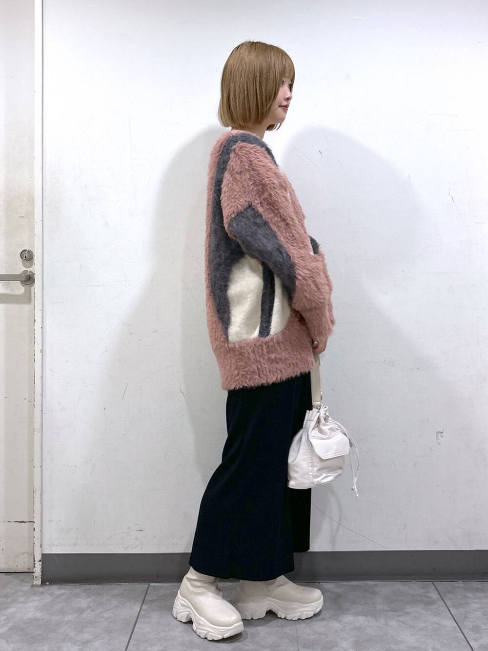 ブラック系のスカート、ホワイト系のブーツ、ホワイト系のショルダーバッグを着用したレディースの秋コーディネートの2枚目の写真