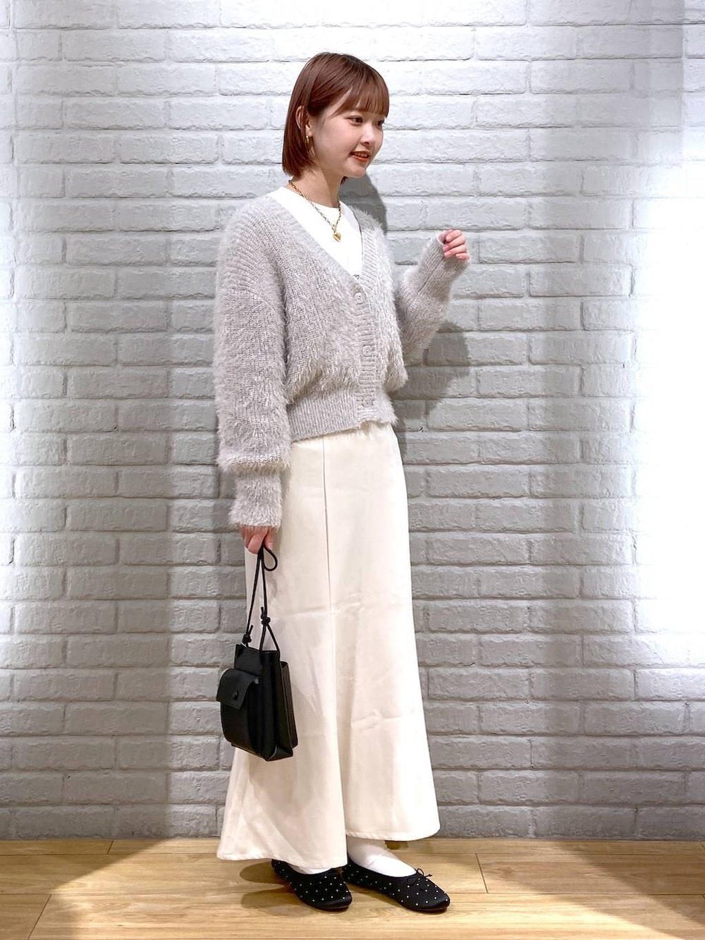 グレー系のニット/セーター、ブラック系のショルダーバッグ、ホワイト系のスカートを着用したレディースの冬コーディネートの2枚目の写真
