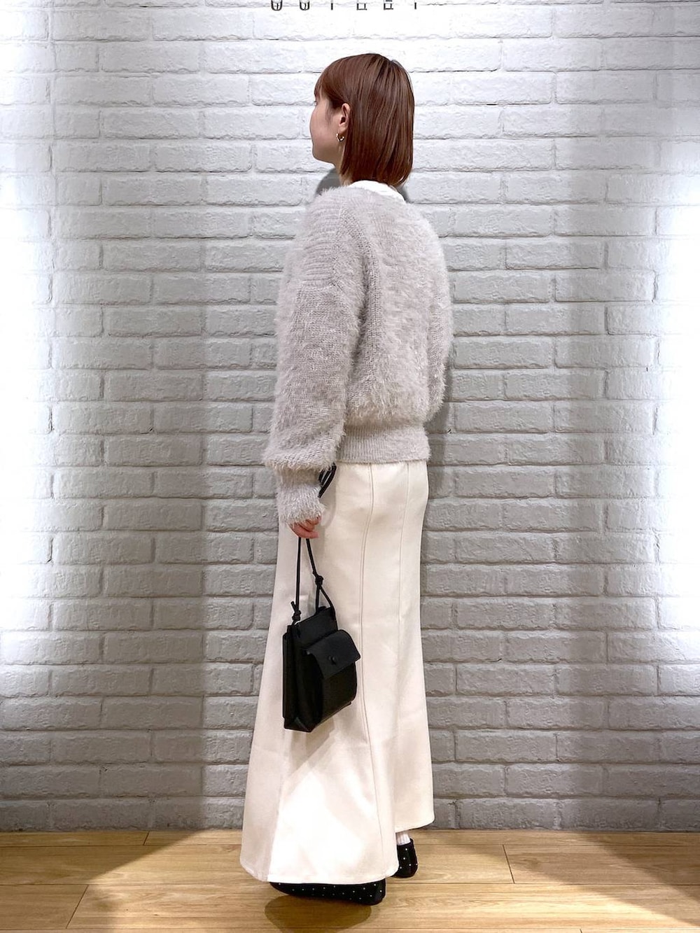 グレー系のニット/セーター、ブラック系のショルダーバッグ、ホワイト系のスカートを着用したレディースの冬コーディネートの3枚目の写真