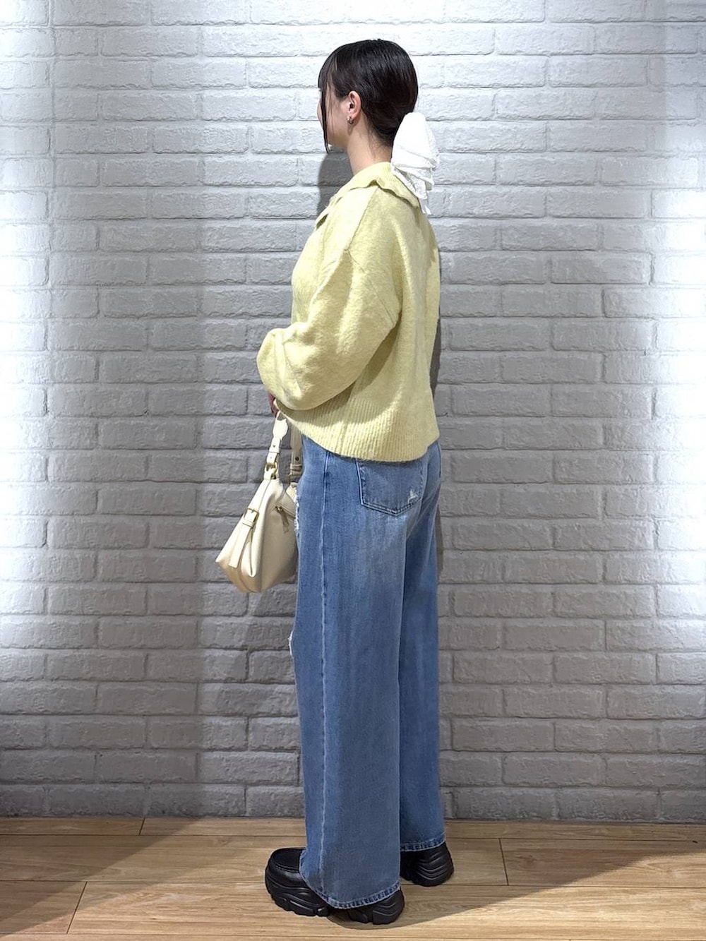 ブラック系のハンドバッグ、イエロー系のニット/セーター、ブルー系のデニムパンツを着用したレディースの秋コーディネートの3枚目の写真