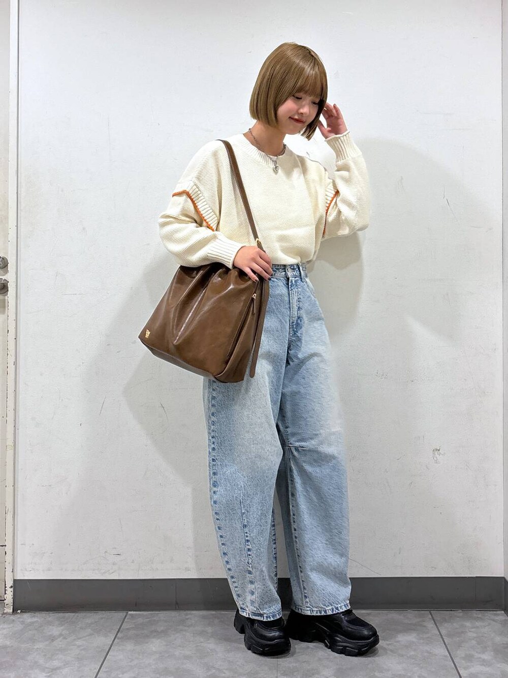 ホワイト系のニット/セーター、ブルー系のデニムパンツ、ブラウン系のショルダーバッグを着用したレディースの秋コーディネートの2枚目の写真