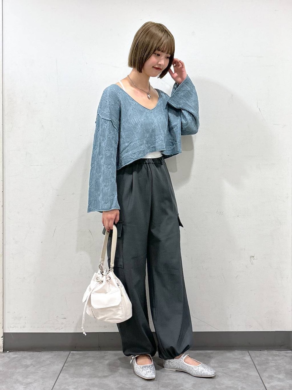 ブルー系のニット/セーター、ホワイト系のショルダーバッグ、グレー系のスラックスを着用したレディースの秋コーディネートの2枚目の写真