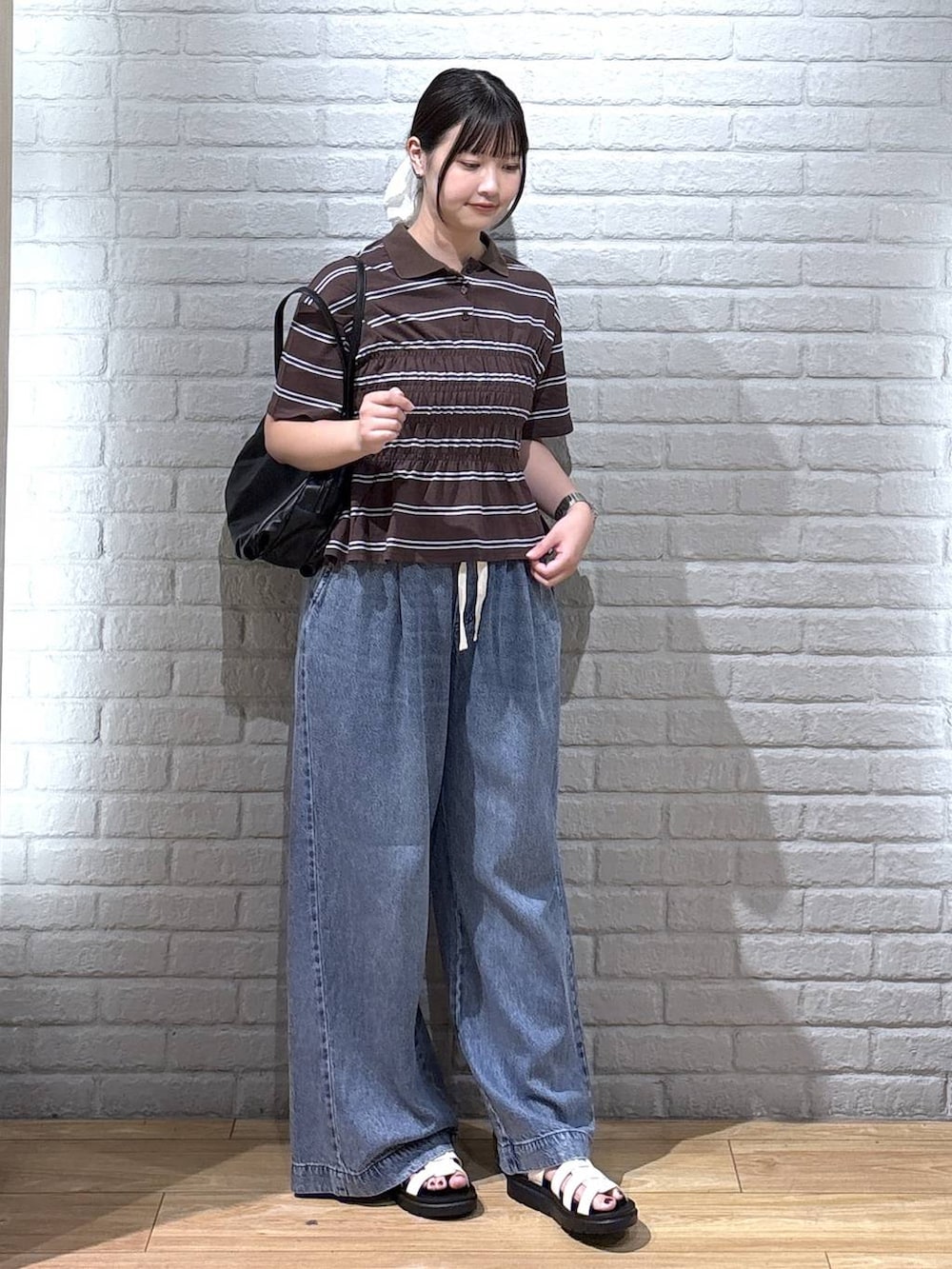 ブラック系のボストンバッグ、ブルー系のデニムパンツ、ホワイト系のサンダルを着用したレディースの夏コーディネートの2枚目の写真