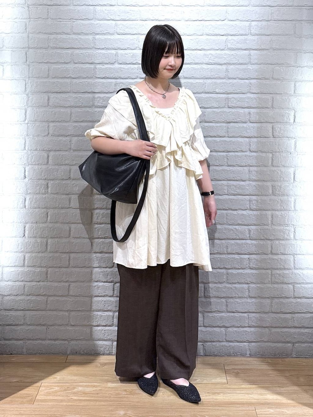 ブラック系のパンプス、ブラウン系のスラックス、ブラック系のショルダーバッグを着用したレディースの夏コーディネートの2枚目の写真