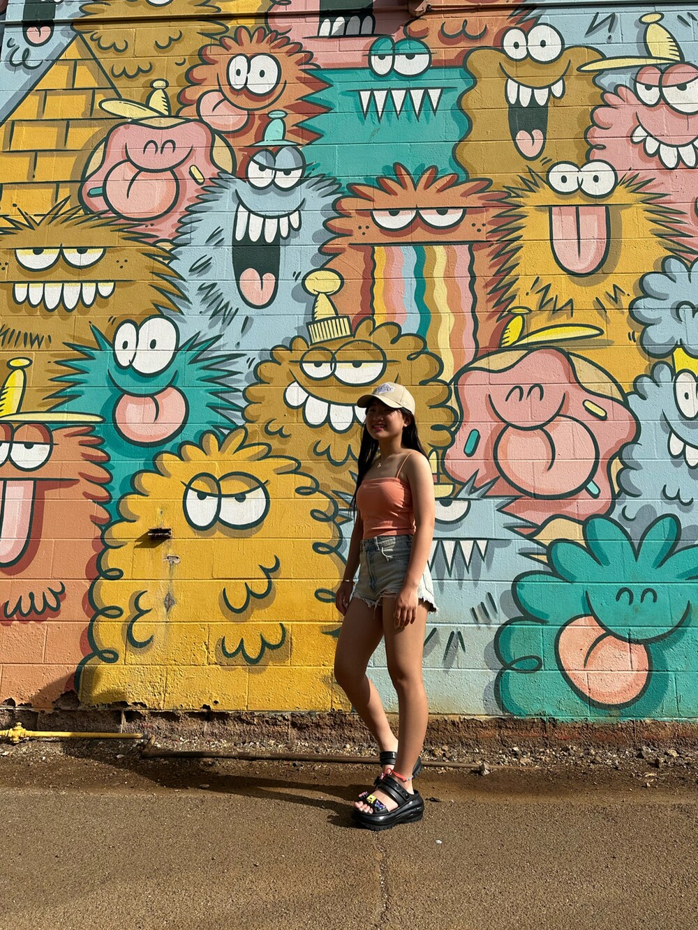 オレンジ系のキャミソール、ブルー系のパンツ、ブラック系のサンダルを着用したレディースの春コーディネートの3枚目の写真