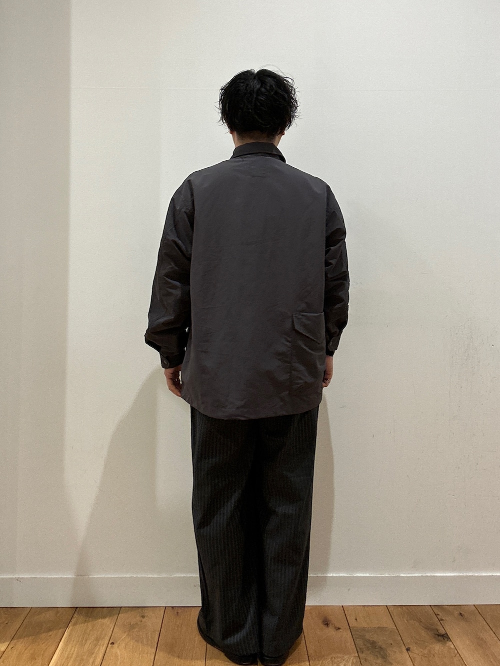 グレー系のスラックス、グレー系のTシャツ/カットソー、グレー系のナイロンジャケットを着用したメンズの春コーディネートの3枚目の写真