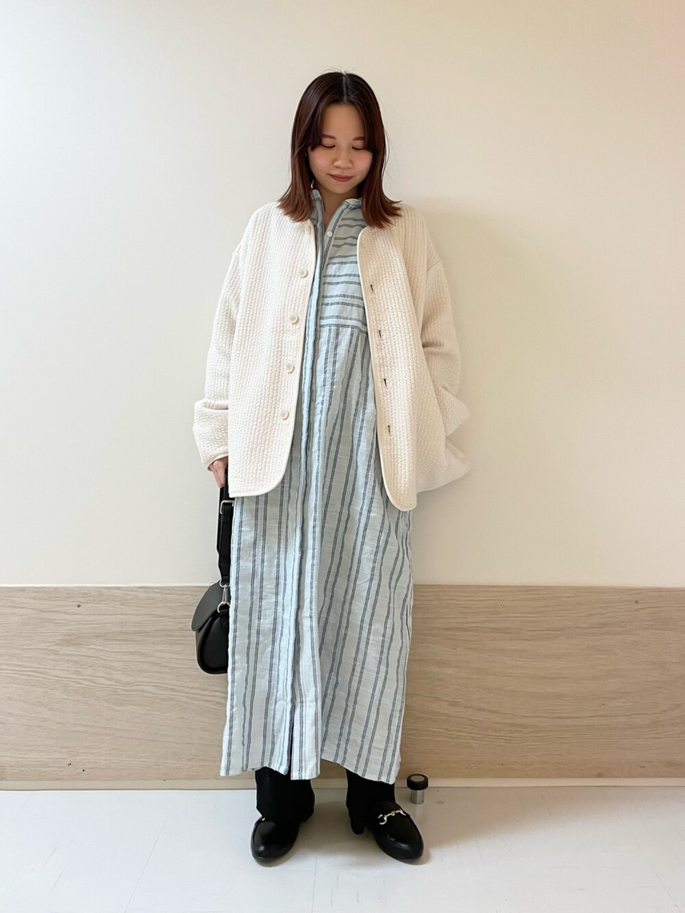 ブラック系のショルダーバッグ、ホワイト系のノーカラージャケット、ブルー系のワンピースを着用したレディースの春コーディネートの2枚目の写真