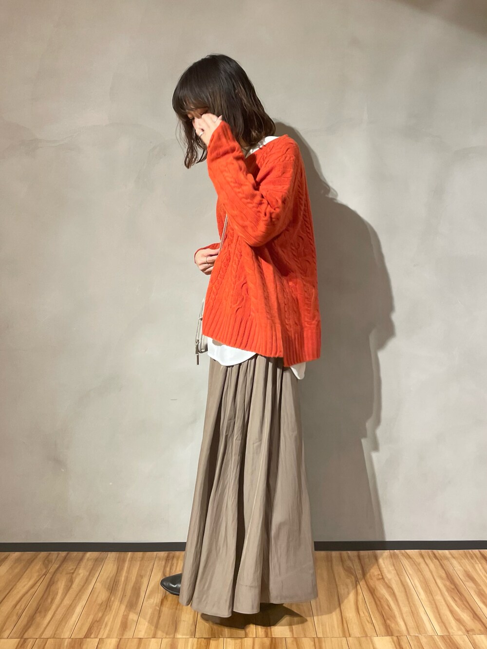 オレンジ系のニット/セーター、ブラウン系のスカート、ブラック系のパンプスを着用したレディースの秋コーディネートの2枚目の写真