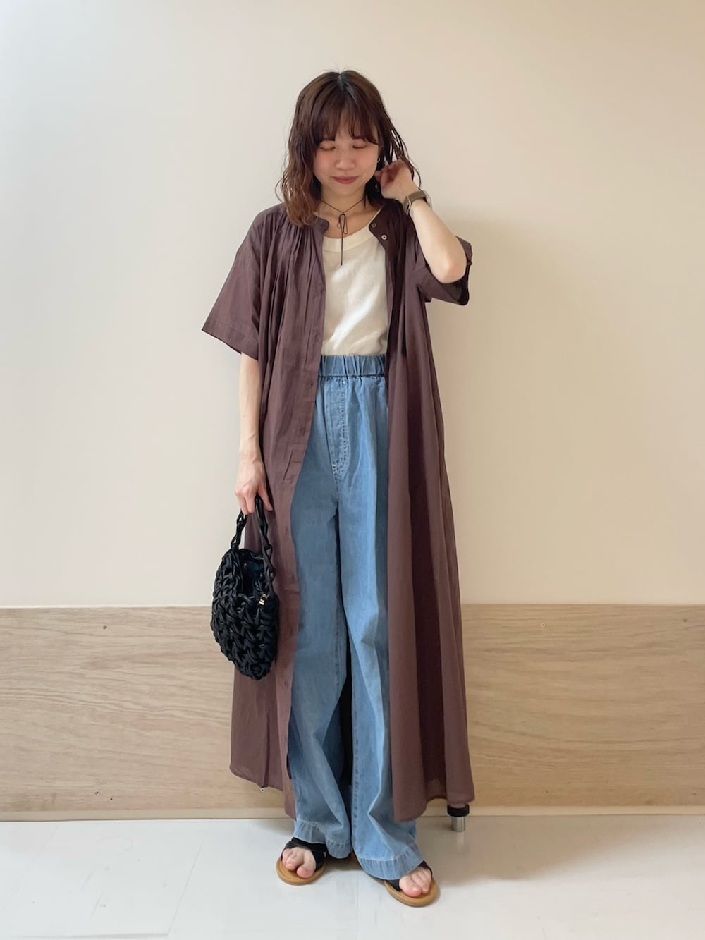 ブルー系のデニムパンツ、ブラック系のサンダル、ブラウン系のワンピースを着用したレディースの春コーディネートの2枚目の写真