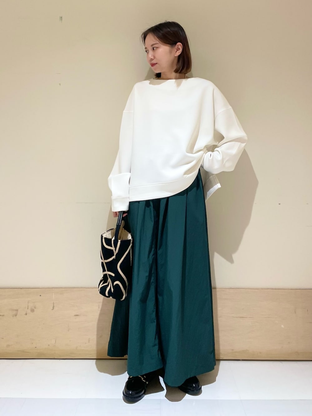 ブラック系のショルダーバッグ、グリーン系のスカート、ブラック系のレインシューズを着用したレディースの秋コーディネートの3枚目の写真