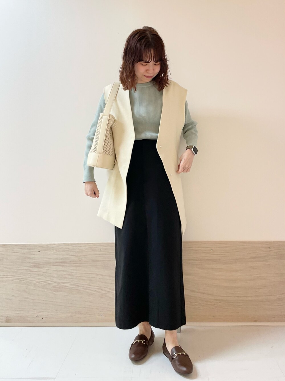 グリーン系のニット/セーター、ホワイト系のその他アウター、ブラック系のスカートを着用したレディースの春コーディネートの2枚目の写真
