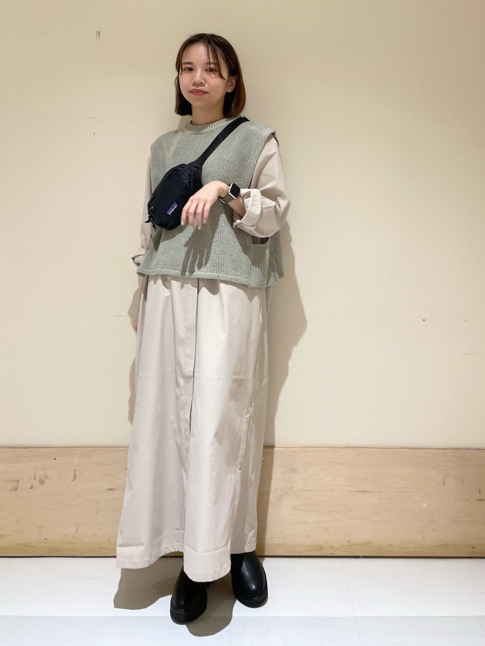 グレー系のワンピース、ブラック系のブーツ、グレー系のベストを着用したレディースの秋コーディネートの2枚目の写真