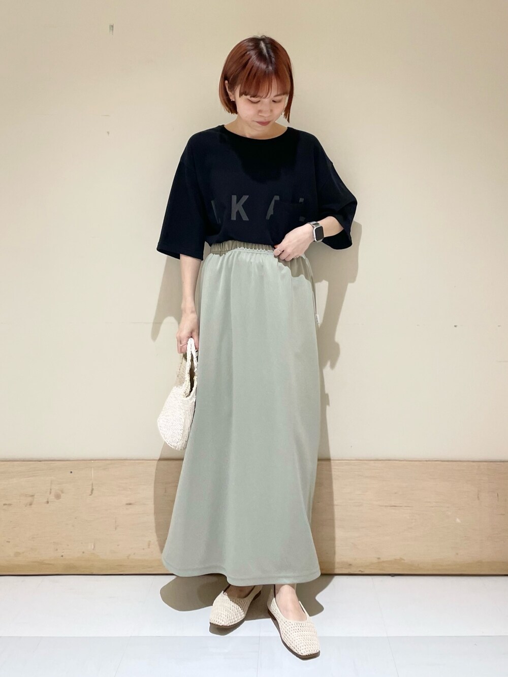 グリーン系のスカート、ブラック系のTシャツ/カットソー、ホワイト系のハンドバッグを着用したレディースの春コーディネートの2枚目の写真