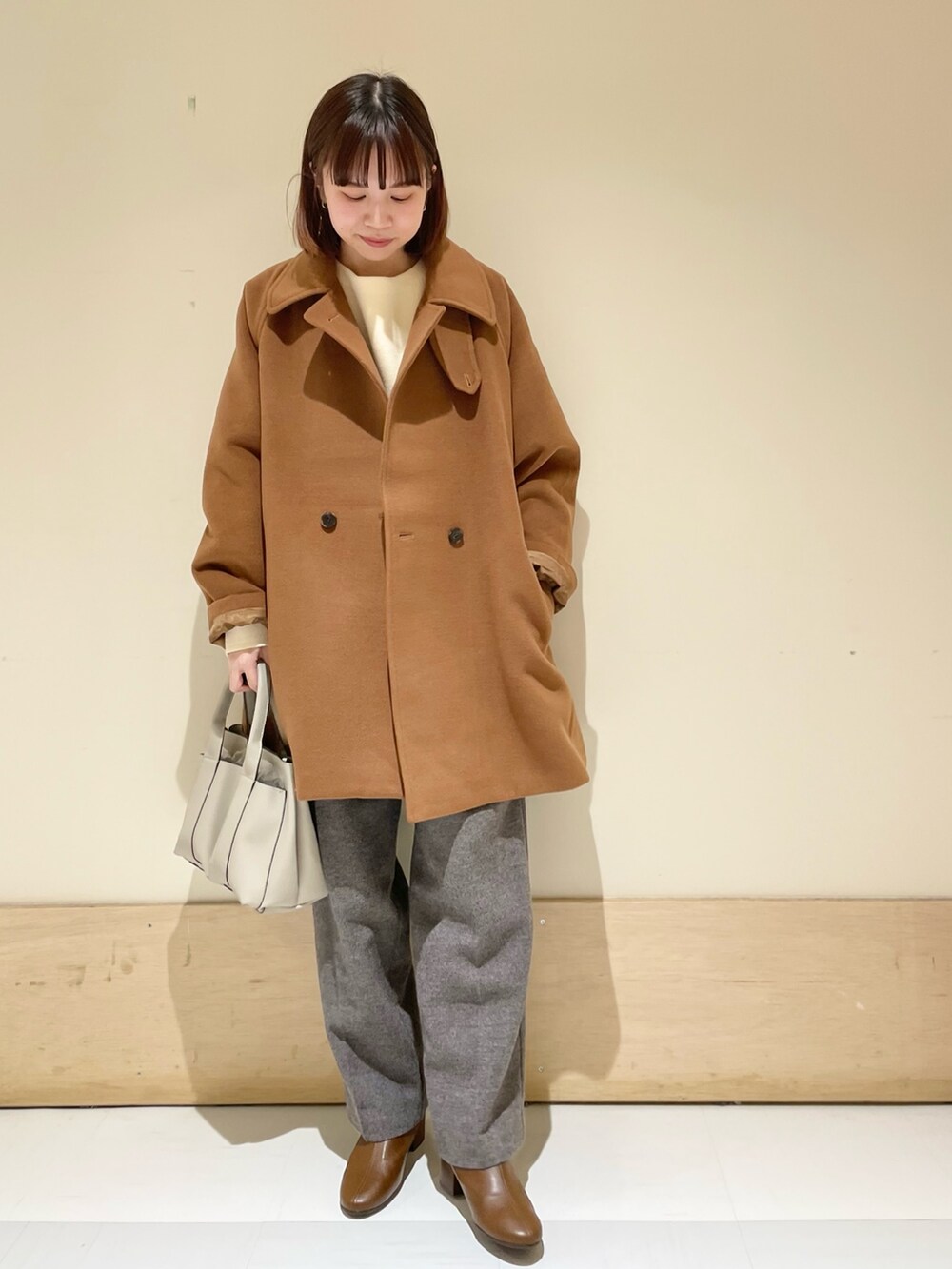 イエロー系のピーコート、ホワイト系のニット/セーター、グレー系のその他パンツを着用したレディースの冬コーディネートの3枚目の写真