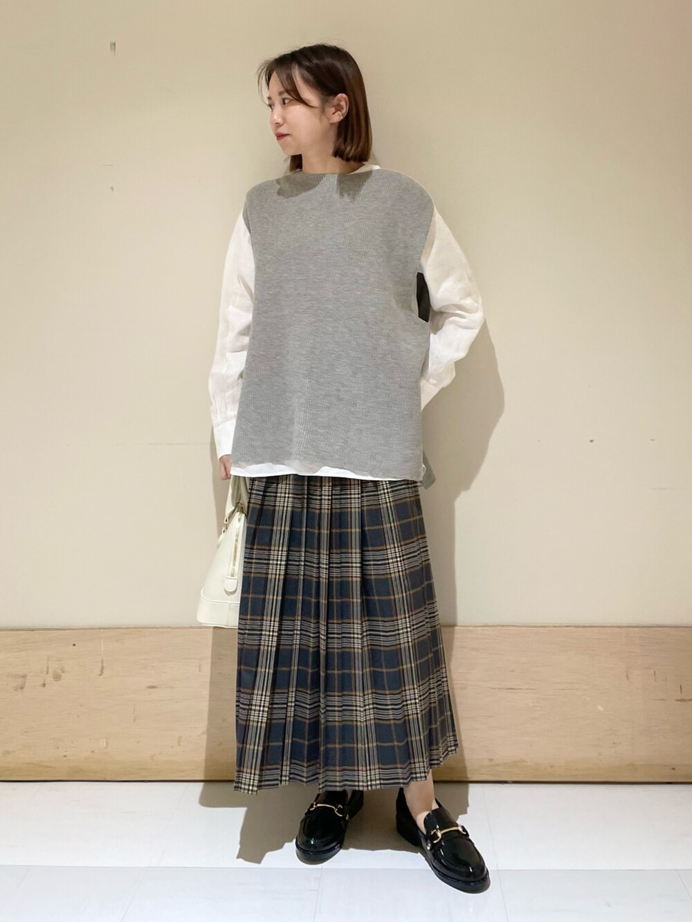 グレー系のベスト、ホワイト系のTシャツ/カットソー、ブラック系のレインシューズを着用したレディースの秋コーディネートの2枚目の写真