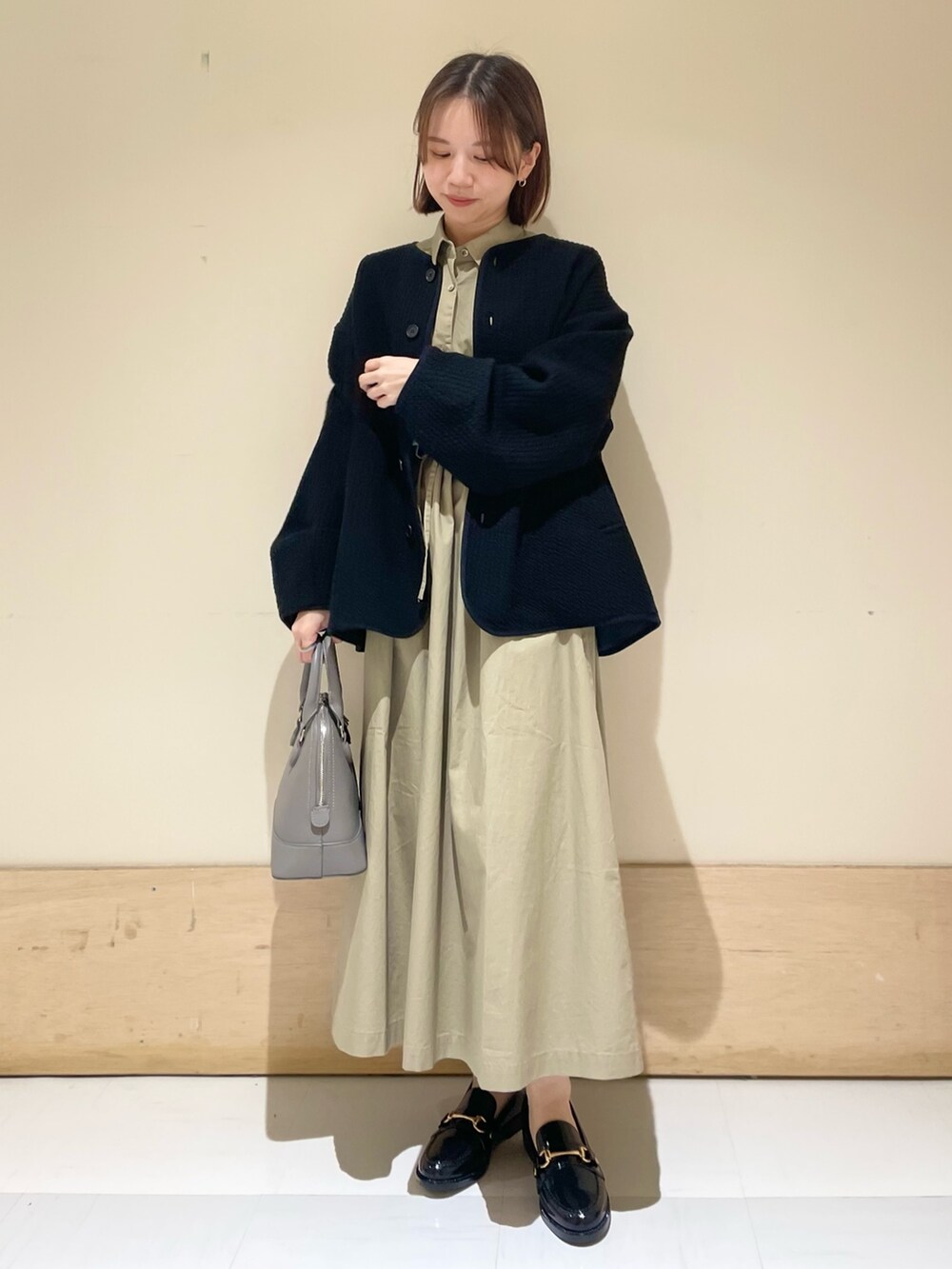 グレー系のショルダーバッグ、ブラック系のノーカラージャケット、ベージュ系のワンピースを着用したレディースの秋コーディネートの3枚目の写真