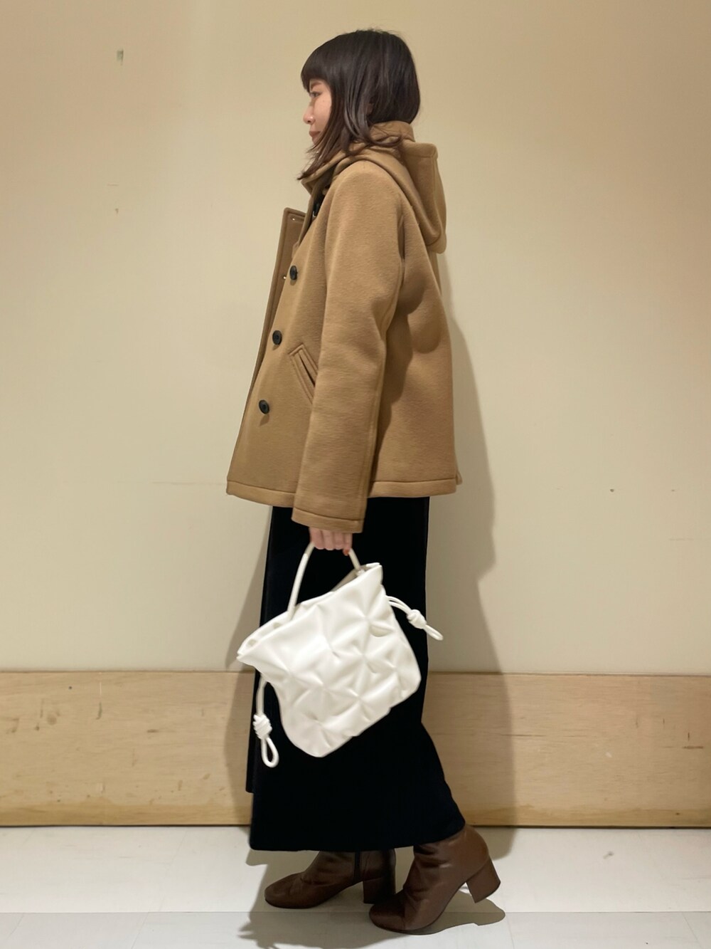 イエロー系のピーコート、ブラック系のワンピース、ブラウン系のブーツを着用したレディースの冬コーディネートの2枚目の写真